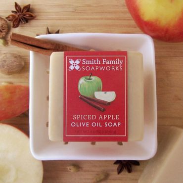 Spiced apple bar soap with red apples, a ceramic berry basket, whole cinnamon, nutmeg, and anise.