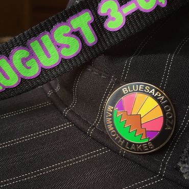 A lanyard and a rainbow sunset enamel pin on a brimmed hat.