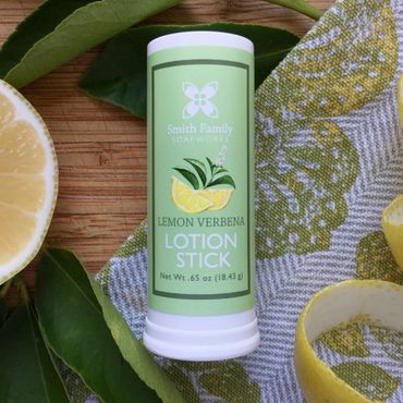 Lemon verbena lotion stick with lemon half, lemon rind, citrus leaves, and tea towel.