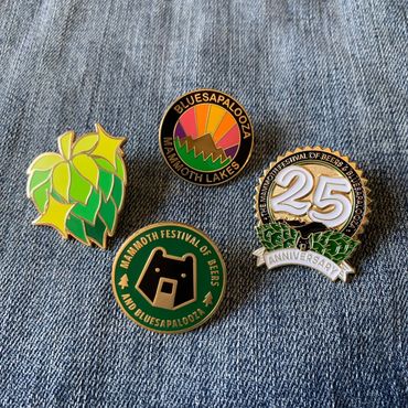Four enamel pins. A sparkly hop, a black bear, a rainbow sunset, and a 25th anniversary design.