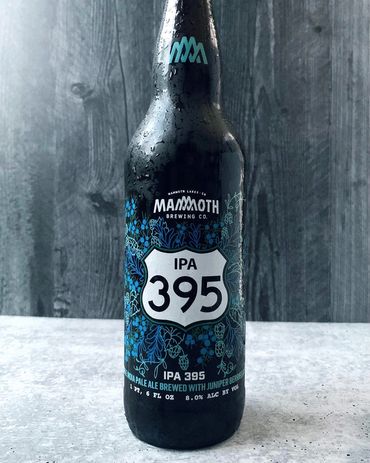 Mammoth Brewing IPA 395 bottle featuring large highway sign with beer name, surrounded by foliage.