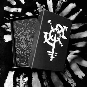 Deck box with brushed sigil. Card back with geometric lines, stars, planets, and a pair of skulls.
