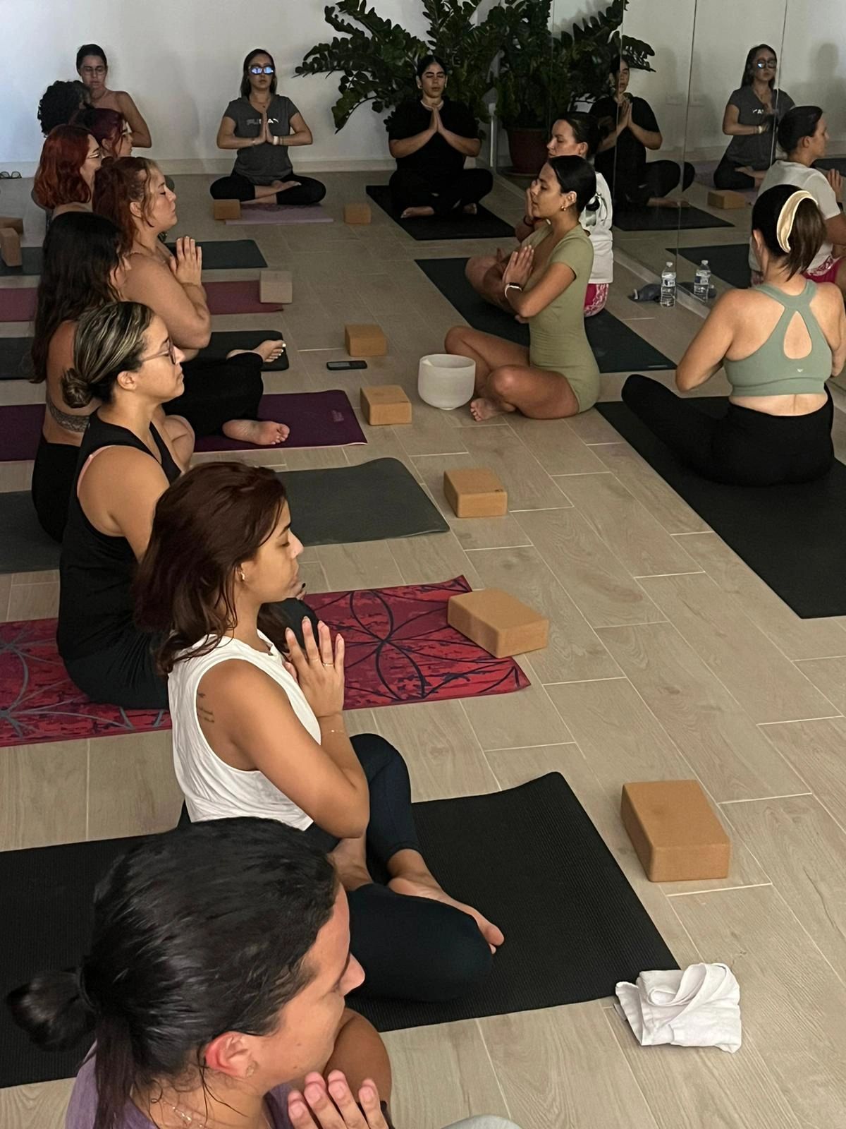 Group meditation session in a serene yoga studio with participants in seated prayer pose.