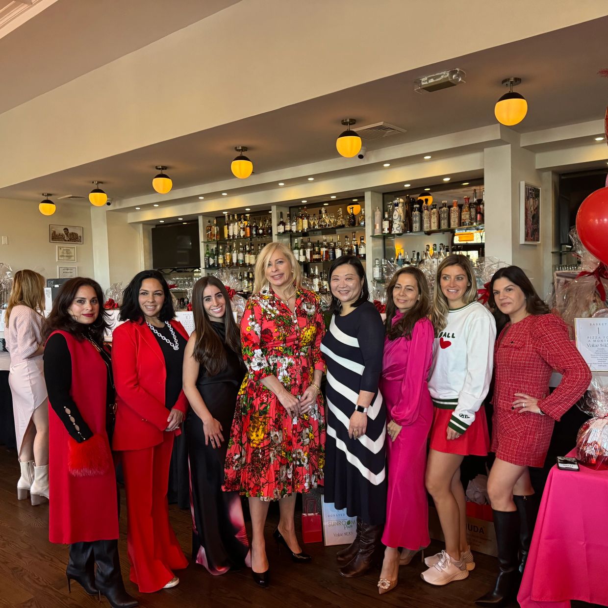 Group of eight diverse women dressed stylishly posing inside a bar.