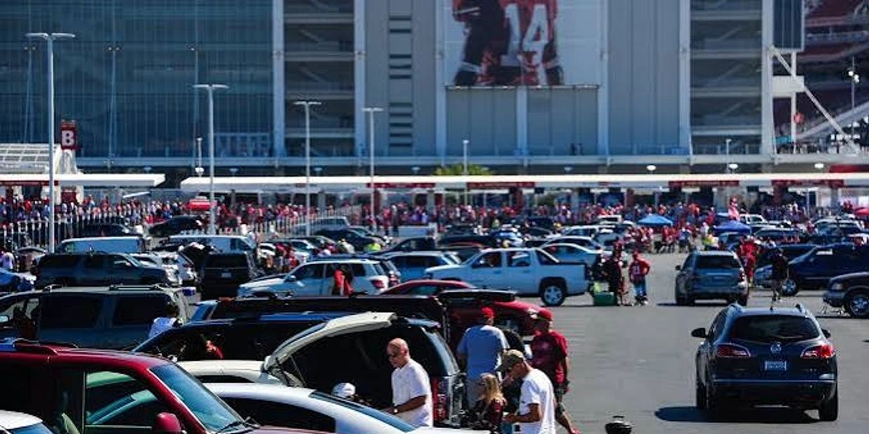 Crowded stadium parking lot with many cars and people.