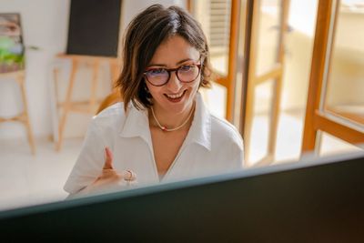 Smiling woman wearing glasses gives a thumbs-up during a video call.