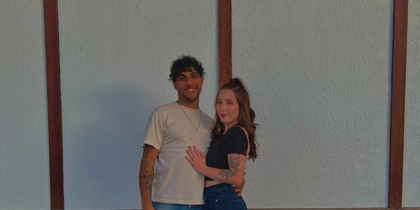 A couple posing happily against a brick and white wall background.