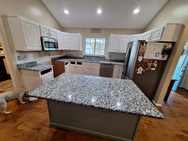 Modern kitchen with granite countertops, white cabinets, and a dog drinking water.