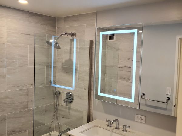 Modern bathroom with illuminated mirror and glass shower screen.