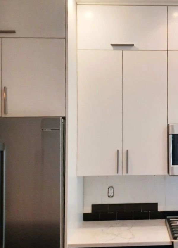 Modern kitchen with white and navy cabinets, stainless steel appliances, and marble countertops.