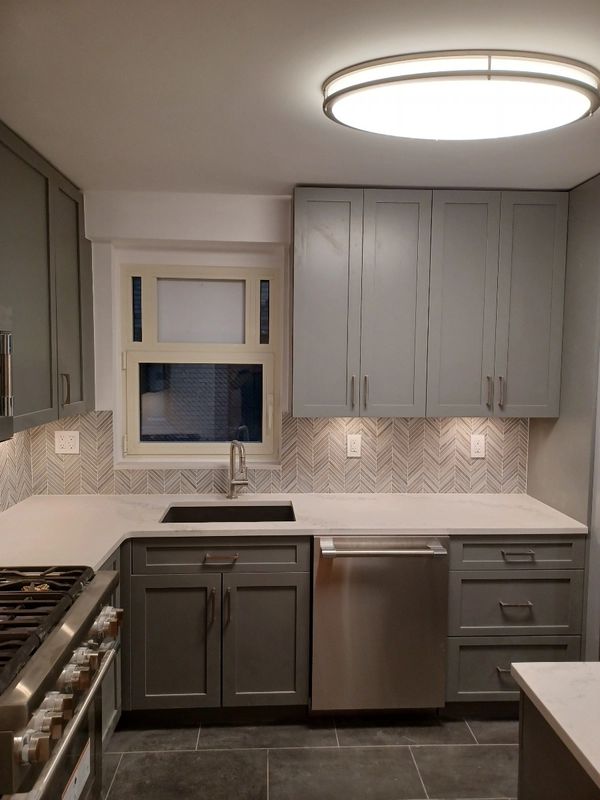 Modern kitchen with gray cabinets, a stainless steel dishwasher, and a geometric backsplash.