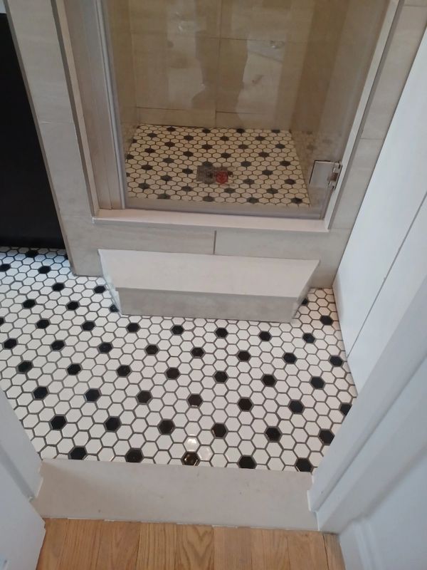 Bathroom floor and shower with black and white hexagonal tiles.