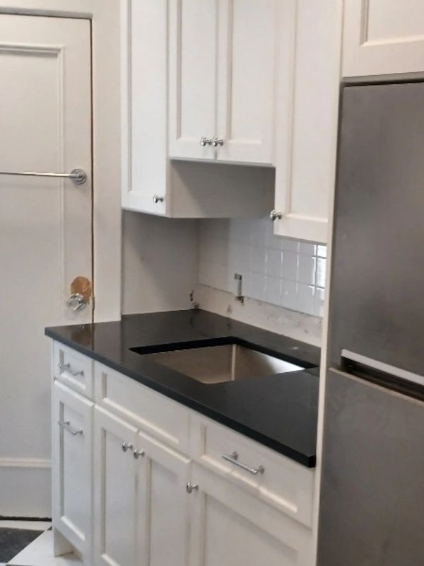 Modern kitchen with white cabinets, black countertop, and stainless steel refrigerator.
