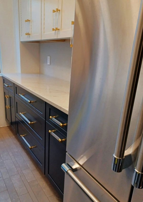 Modern kitchen with black and white cabinets, gold handles, and stainless steel refrigerator.
