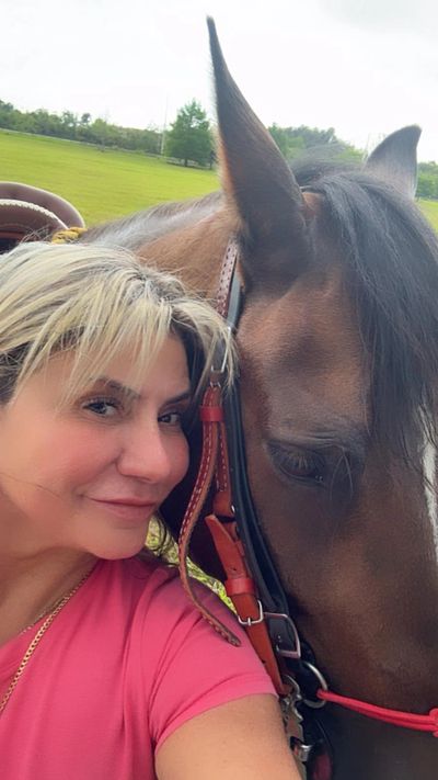 Woman in pink taking a close selfie with a brown horse outdoors.
