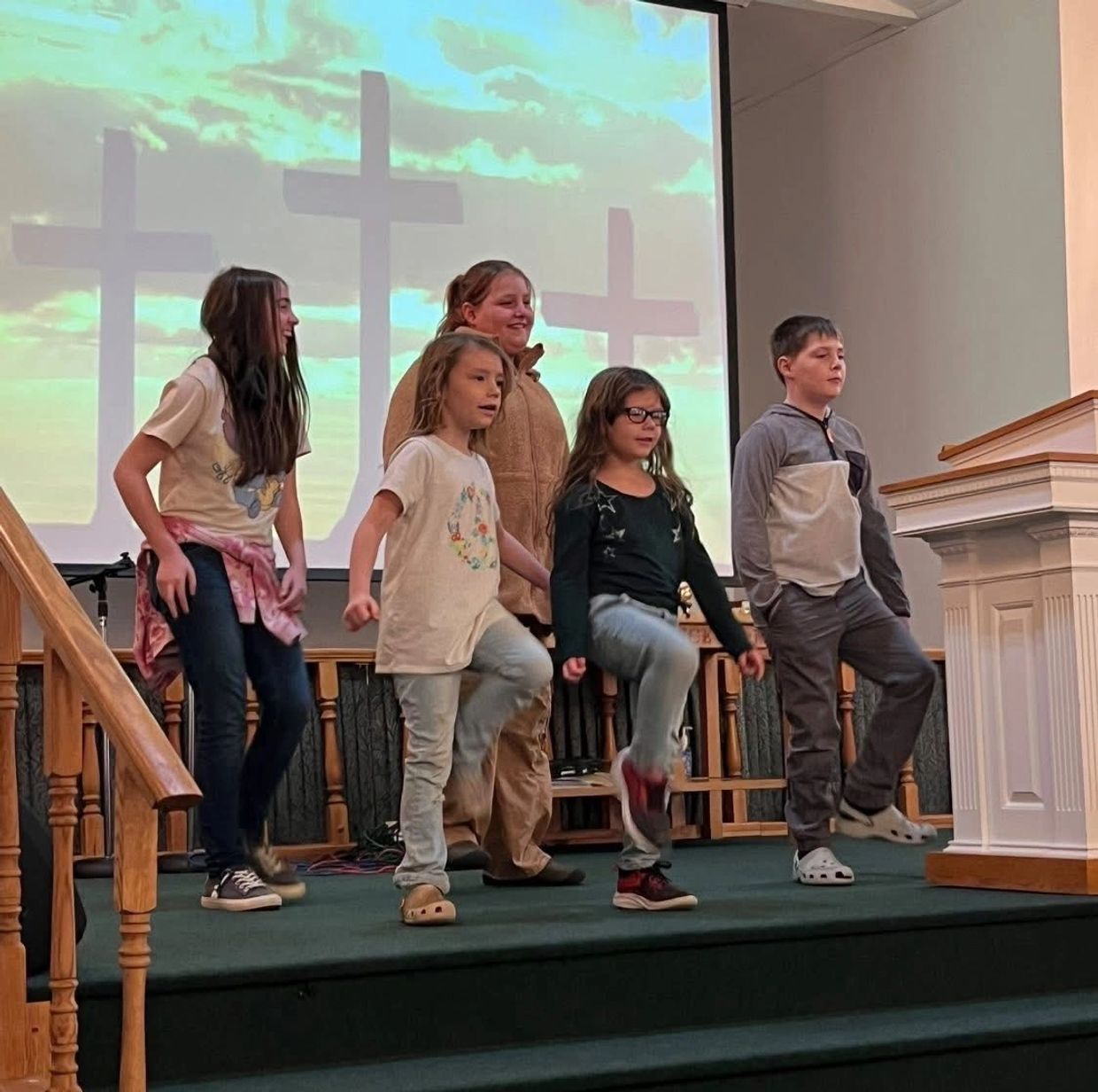 Group of kids dancing on stage in church with crosses in background.