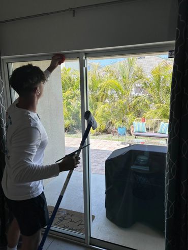 A person cleaning a sliding glass door with a mop and cloth.