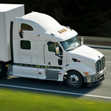 White semi-truck driving on a highway with green grass beside the road.