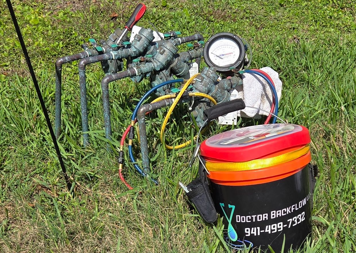 Backflow testing equipment setup in grassy area with labeled bucket.