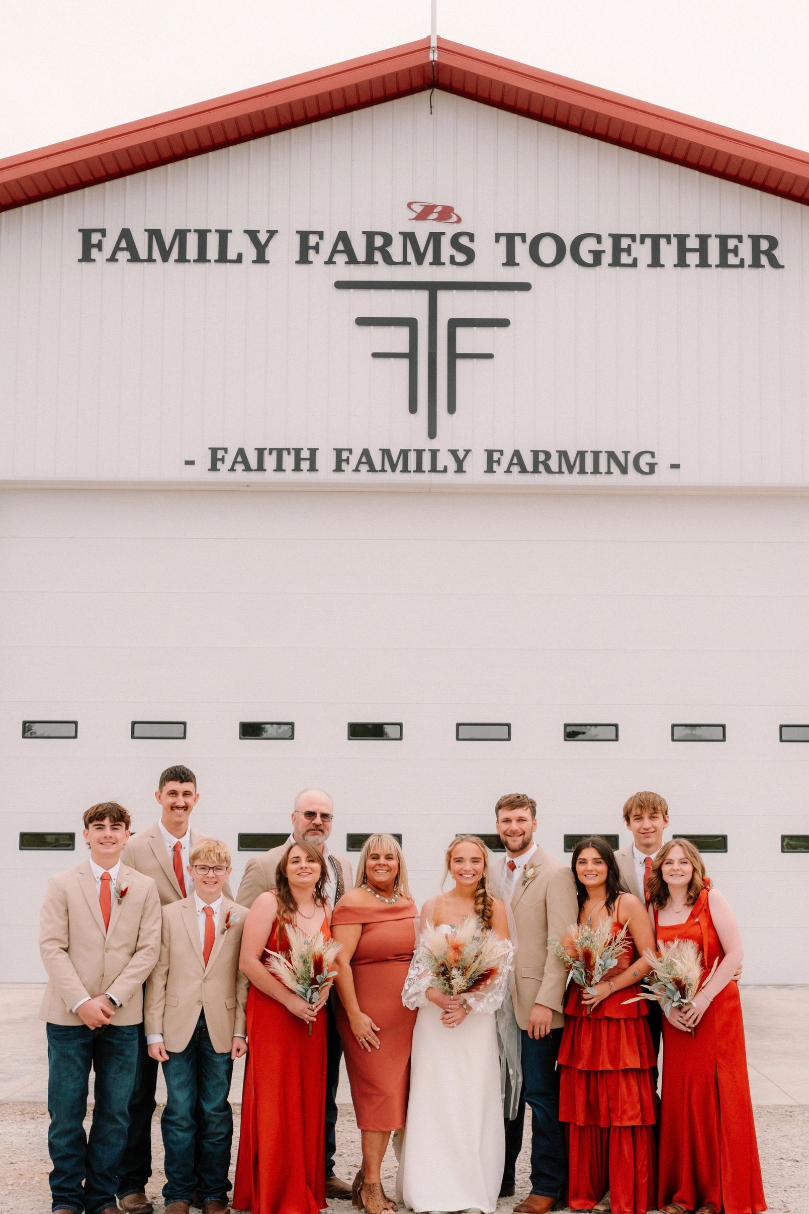 Family wedding group in coordinated attire in front of a farm building.