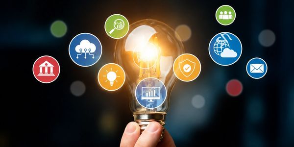 Hand holding a glowing light bulb with business icons around.