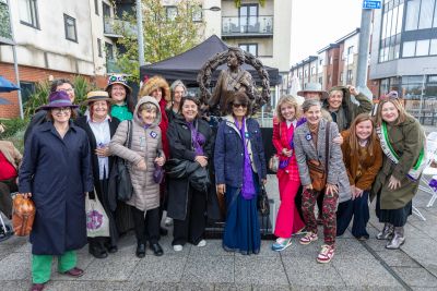 Group of people posing with a statue outdoors in an urban area.