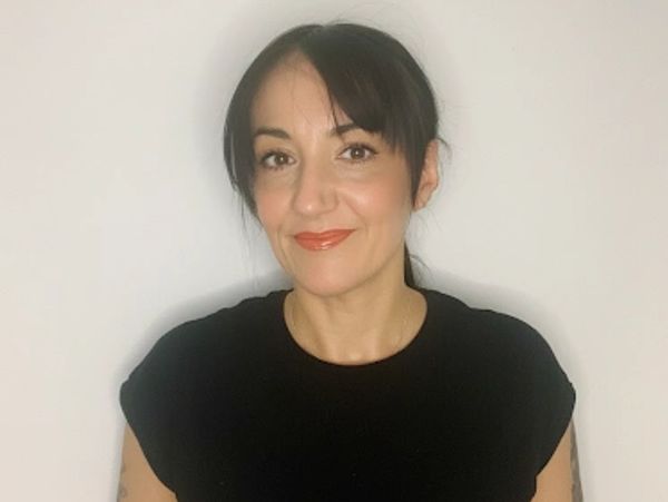 Woman in a black shirt smiling against a plain white background.