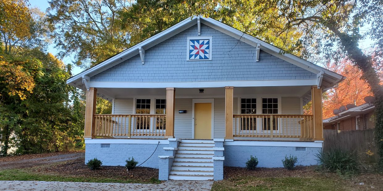 Blue and white house with a yellow door and wooden porch railings.