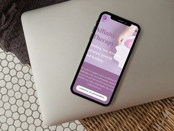 alt="Affinity Therapy webpage on phone on top of a laptop"