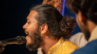 Man singing into a microphone with a man bun hairstyle.