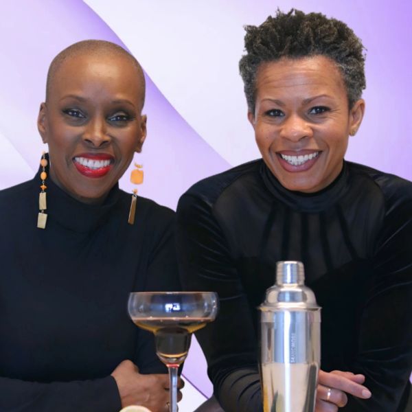 Two women smiling, sitting with cocktail glass and shaker.