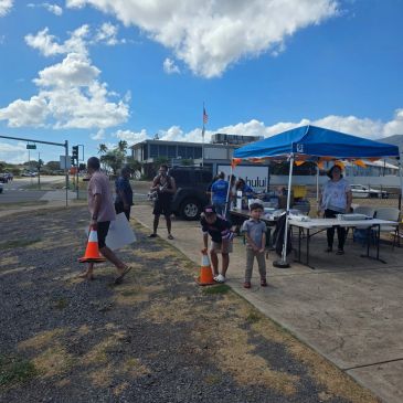 People at an outdoor event with a tent and signage.