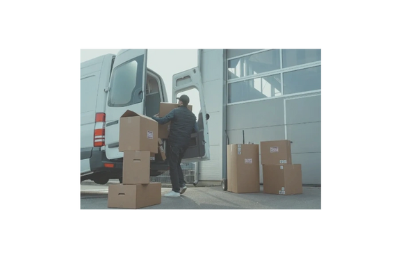 Man loading cardboard boxes into a delivery van outside a warehouse.