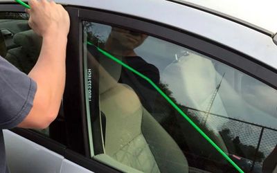 Person using a green tool to unlock a car door window.