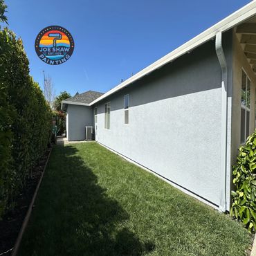 Freshly painted exterior stucco with light gray exterior wall of a house with green lawn and clear blue sky.