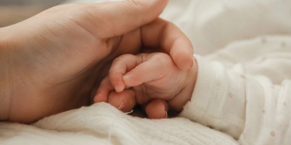 Adult hand gently holding a baby's hand.
