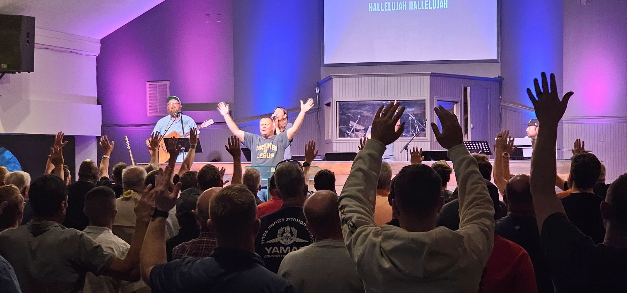 Congregation raising hands in worship during a church service with live music.