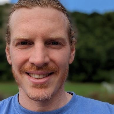 Front angle view of a man with brown hairs smiling at the camera