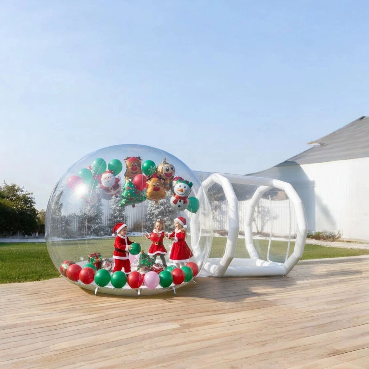 Three children in Christmas costumes inside a transparent inflatable holiday bubble with balloons.