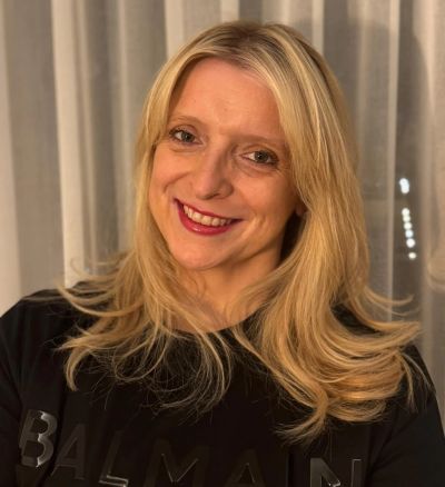Smiling blonde woman in a black Balmain shirt.
