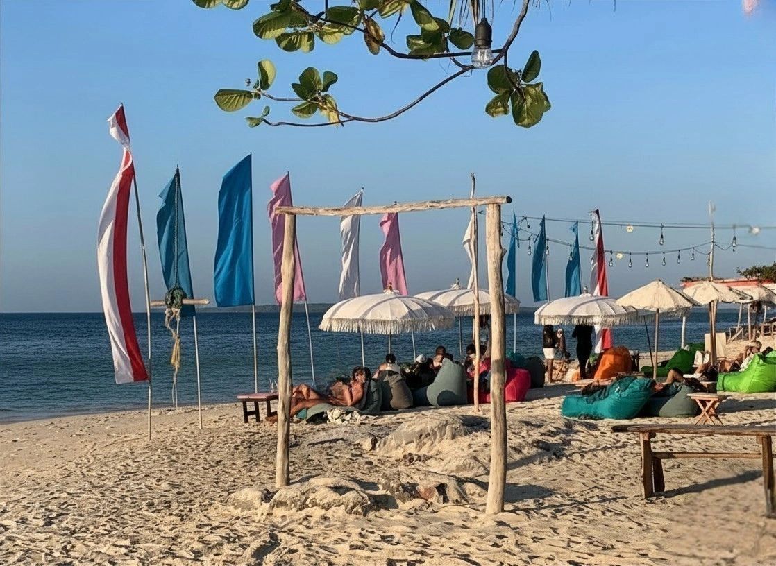 Beach scene with colorful flags, umbrellas, and people relaxing on bean bags.