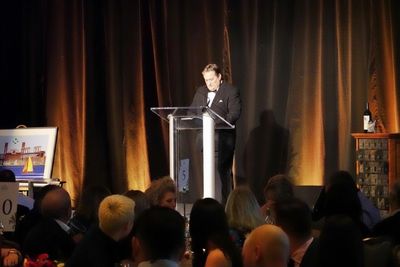 A man in a tuxedo speaking at a podium during a formal event.