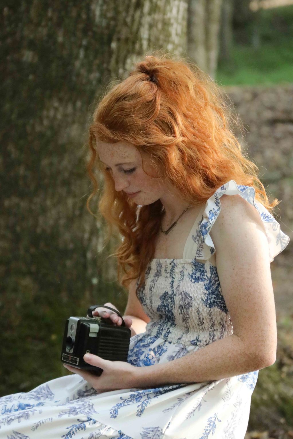 Young woman with red hair holding a vintage camera.
