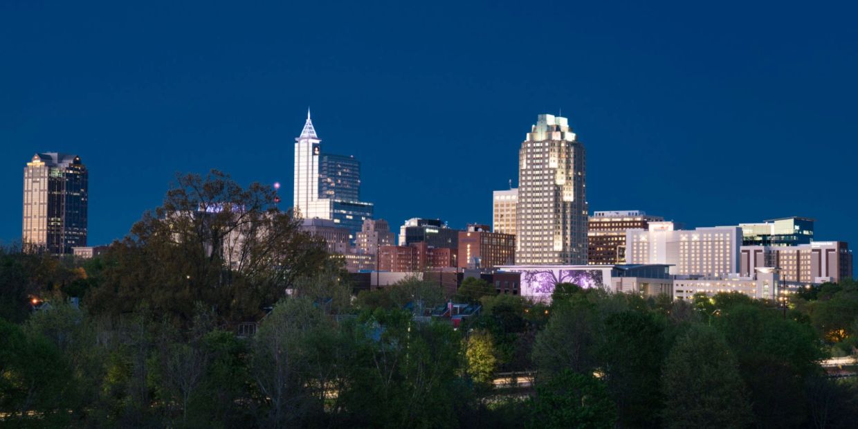 Nighttime city skyline with illuminated buildings and dark blue sky.