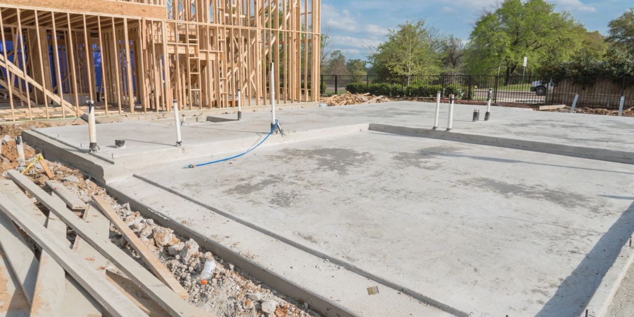 Concrete foundation with plumbing pipes and wooden framing for new construction.