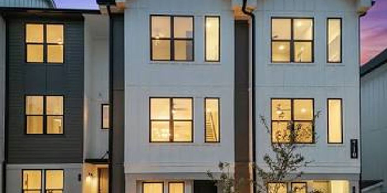 Modern three-story townhouse with illuminated windows at dusk.