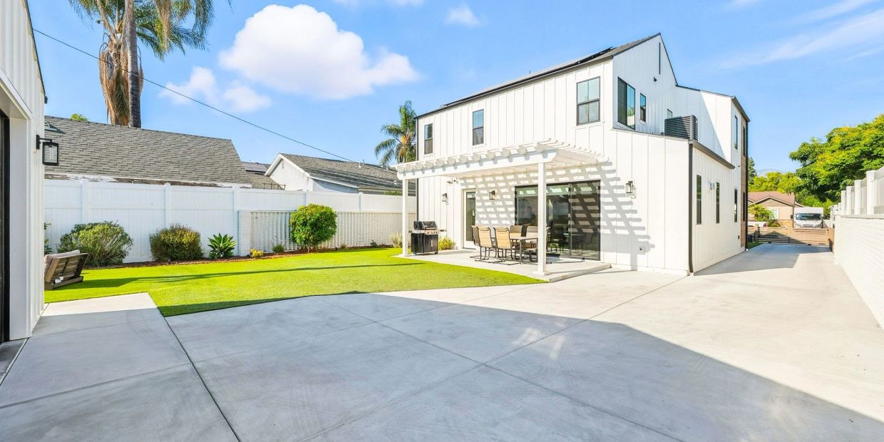 Modern white two-story house with a shaded patio and a spacious concrete driveway.