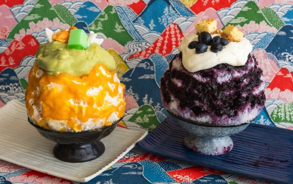 Two colorful shaved ice desserts with toppings on decorative plates.