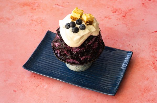 Blueberry shaved ice dessert topped with cream and cake cubes on a blue plate.