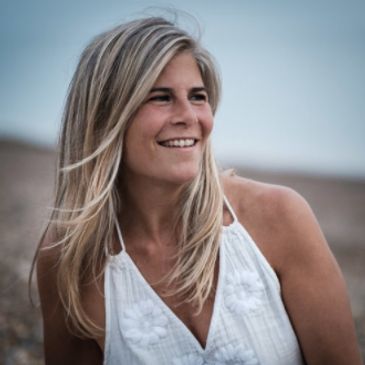 Smiling woman with blonde hair in white dress outdoors.